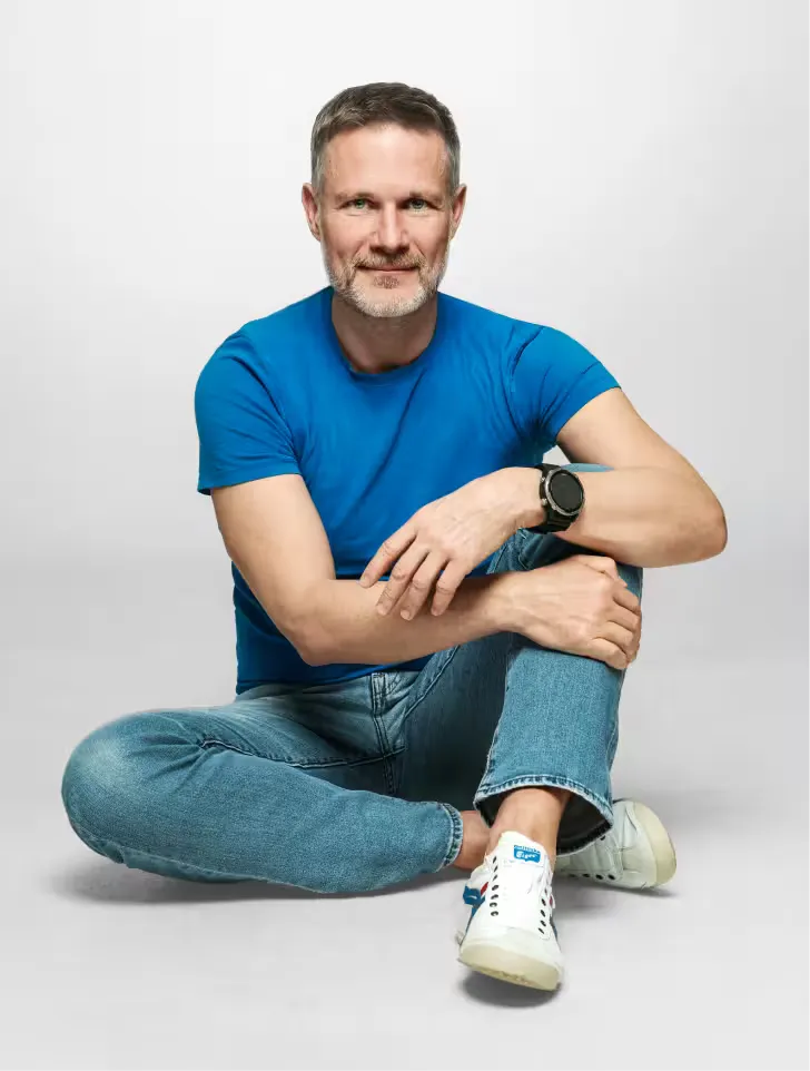 Piotr Urbanik – coach przywódców i liderów biznesu, siedzący w niebieskiej koszulce na szarym tle