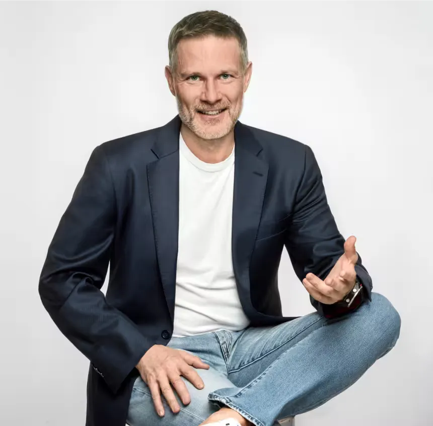 Piotr Urbanik – coach liderów biznesu podczas rozmowy, gestykulujący w granatowej marynarce na jasnym tle